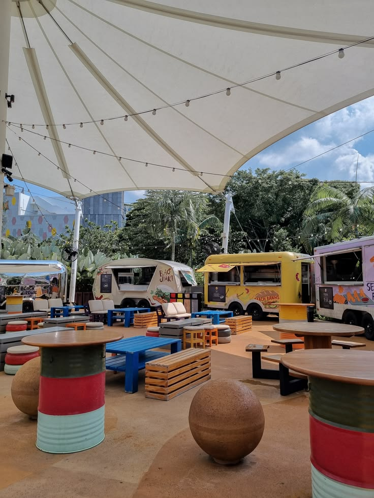 Praça de food trucks ao ar livre com mesas e bancos coloridos, ilustrando o projeto de sinalização Feira Rua Aberta.